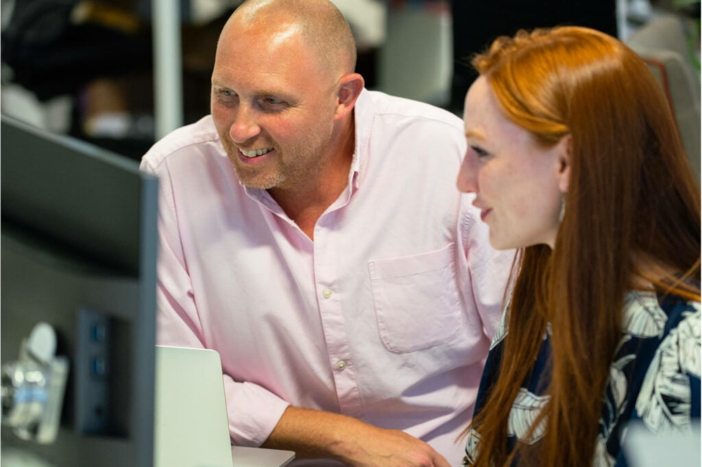 Photograph of a man and woman sitting at computer, in conversation looking happy.